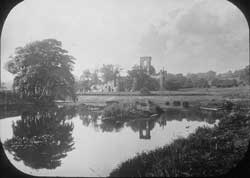 The ruins of Kirkstall Abbey partly masked by trees and other vegetation as seen from the weir before the programme of conservation in 1892-6.